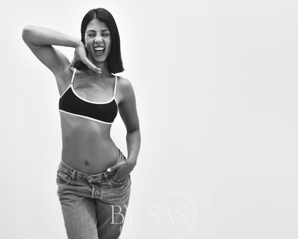Black and white photo of a laughing young woman in a crop top and jeans in a playful pose.