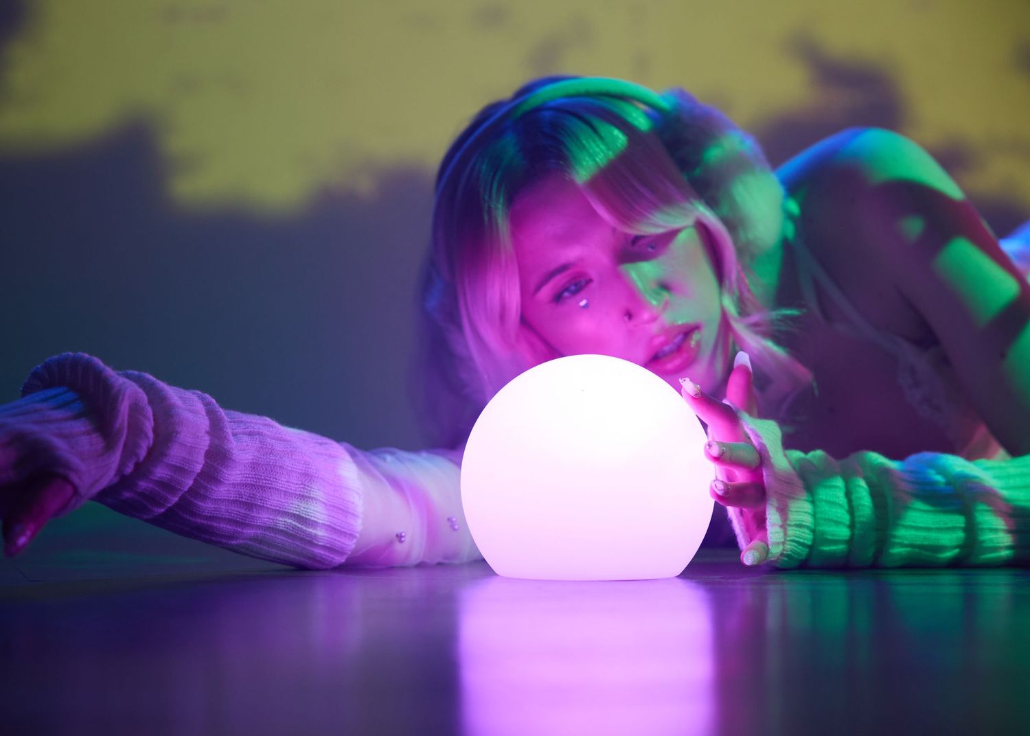 A young woman gazes at a glowing white orb under vibrant purple and green neon lights.