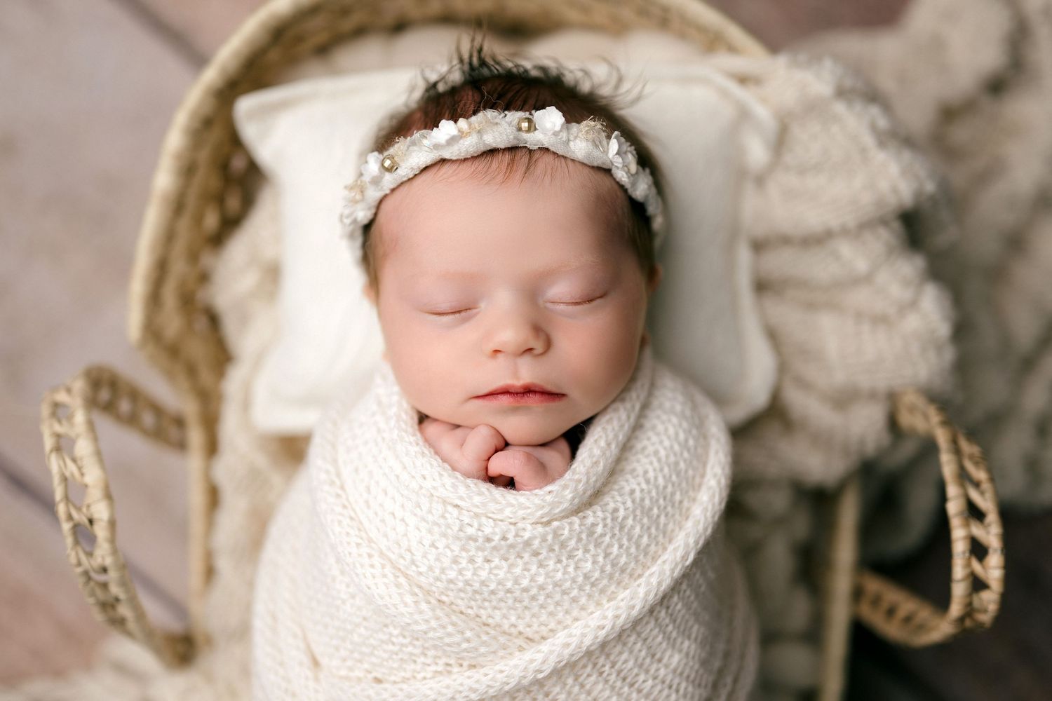 Sleeping newborn baby wrapped in white knit blanket inside a metal bucket with green leaf decorations.