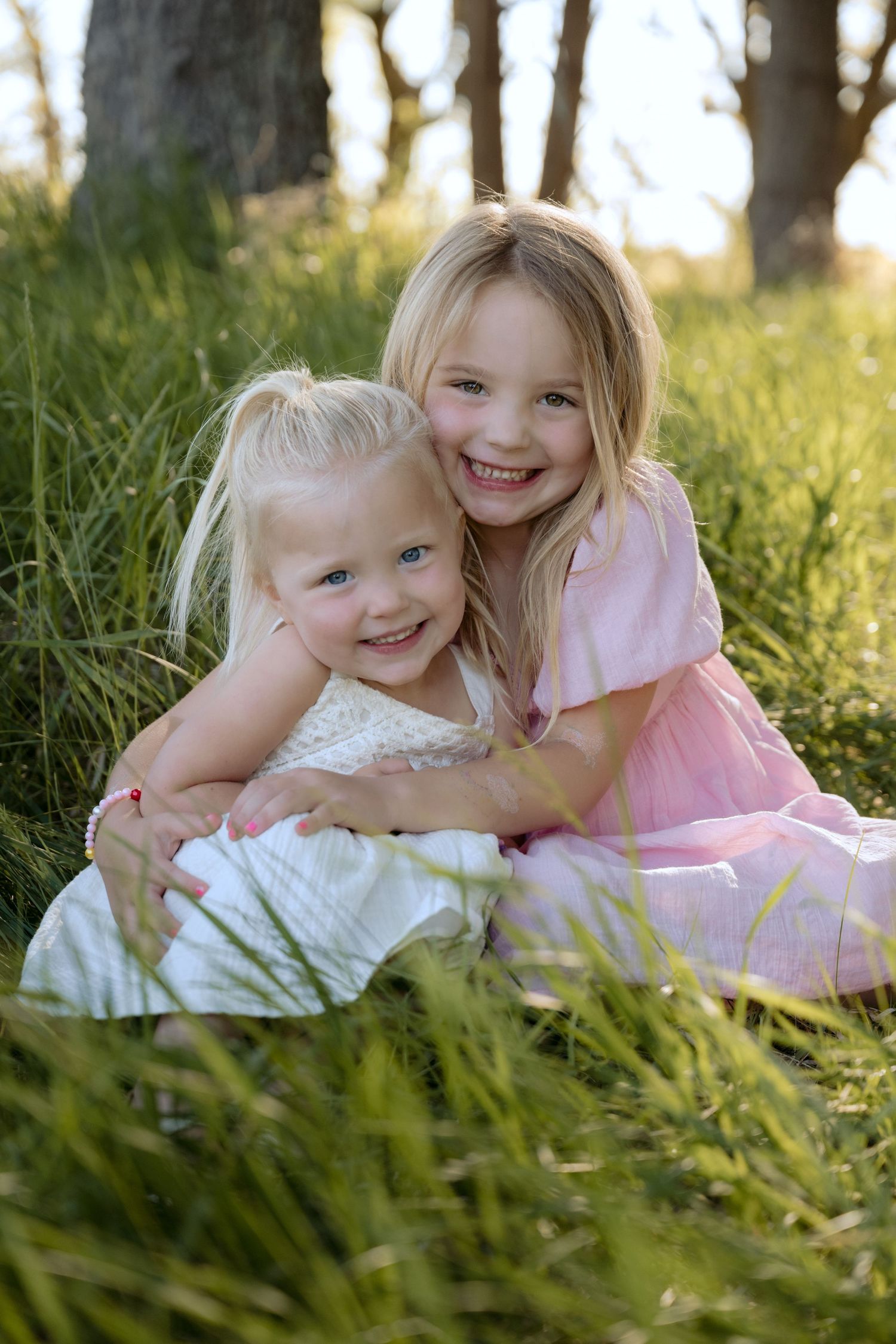 young sisters hug while sitting in the grass for outdoor spring family portraits in hudson, WI