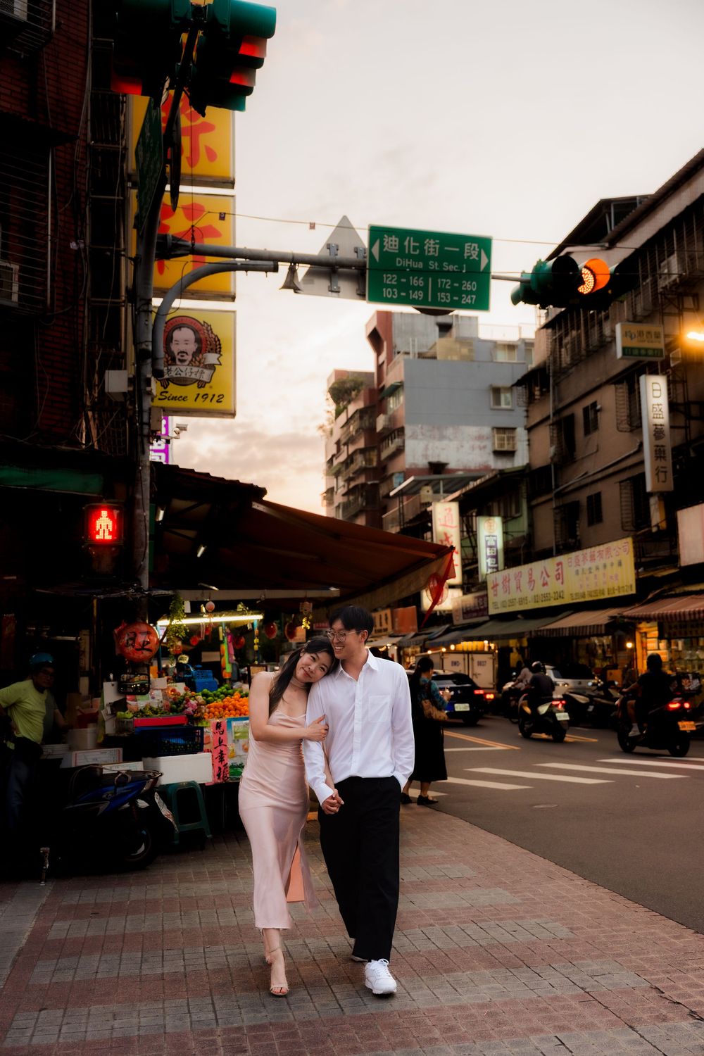 Couple holding hands and walking together on a bustling Taipei street at dusk.