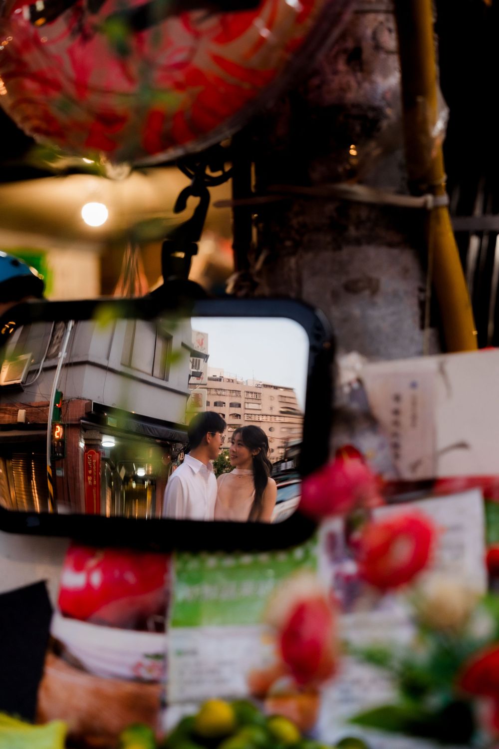 Couple sharing a romantic moment reflected in a vintage side mirror surrounded by colorful flowers.