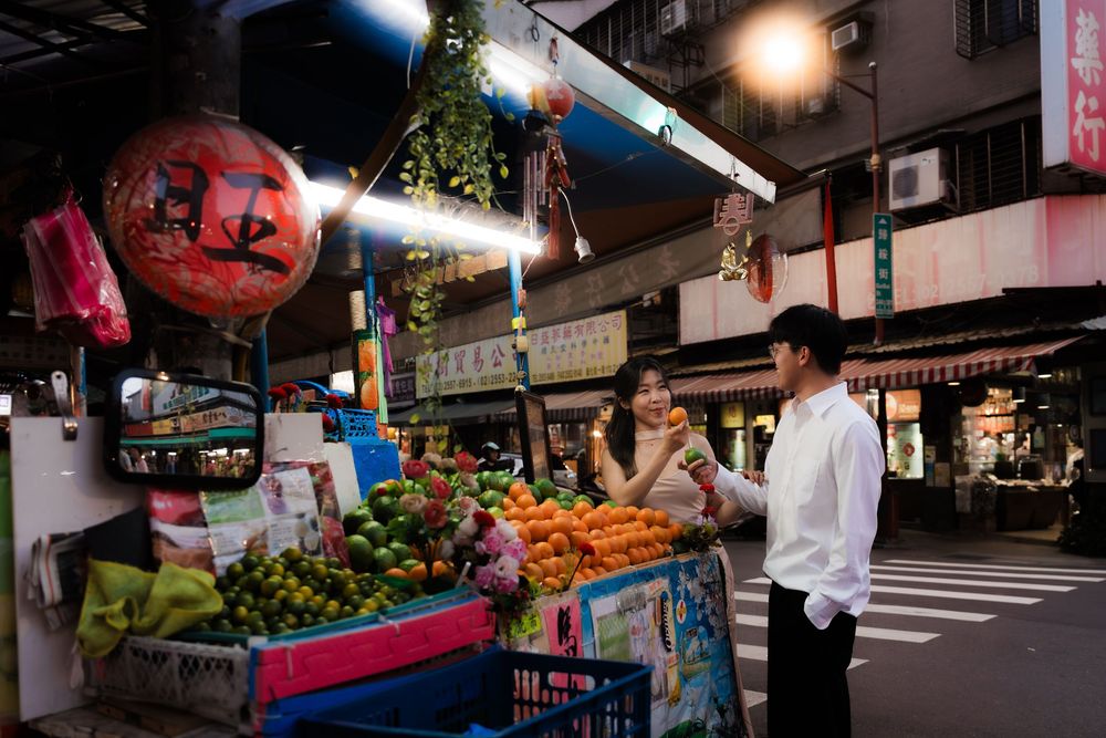 Couple shopping at a vibrant night market fruit stall illuminated by warm lights in Asia.