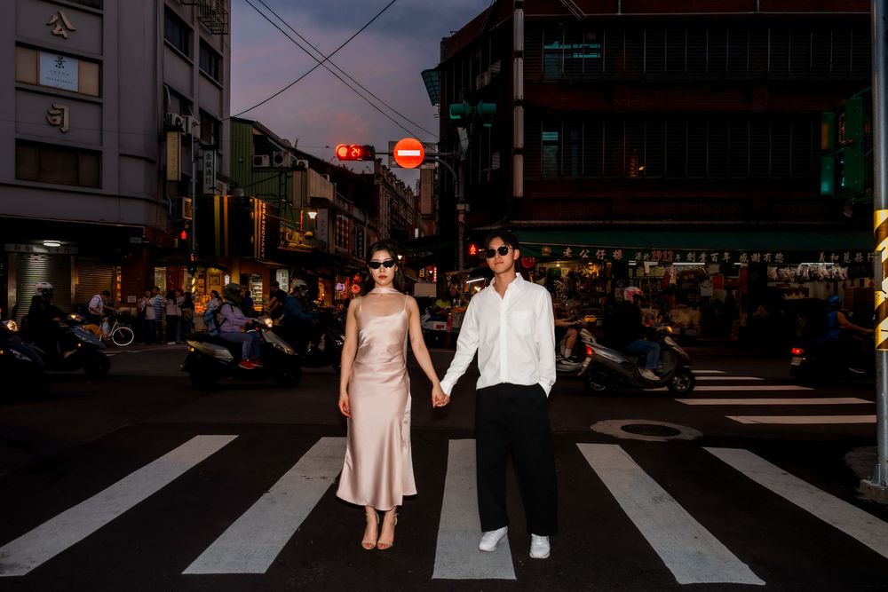 Stylish couple holding hands on a pedestrian crossing at twilight in Taipei.
