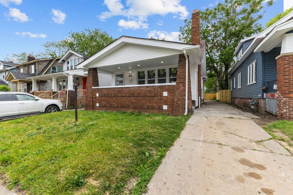 Brick bungalow home with white trim, covered porch, green lawn, and concrete driveway in a residential neighborhood. Detroit Michigan Photo
