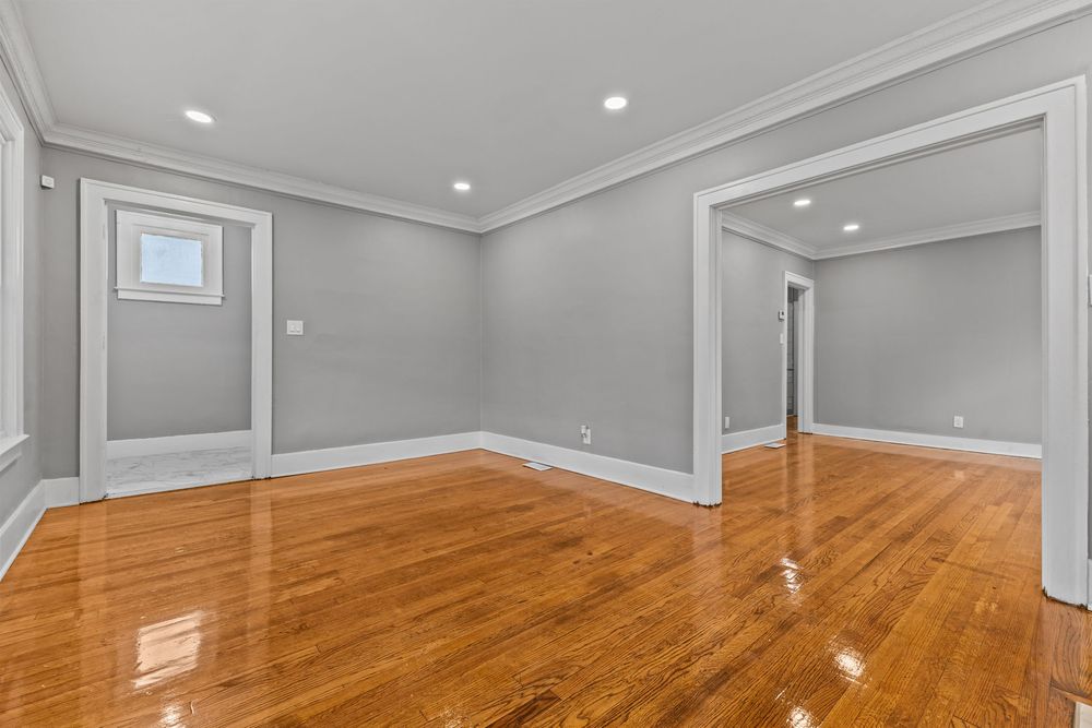 Bright empty room with gleaming hardwood floors, gray walls, crown molding, and recessed lighting in a renovated home. Detroit Michigan Phot