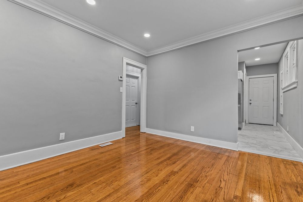 Bright empty room with hardwood floors, gray walls, crown molding, and open doors leading to hallway and closet. Detroit Michigan Photo