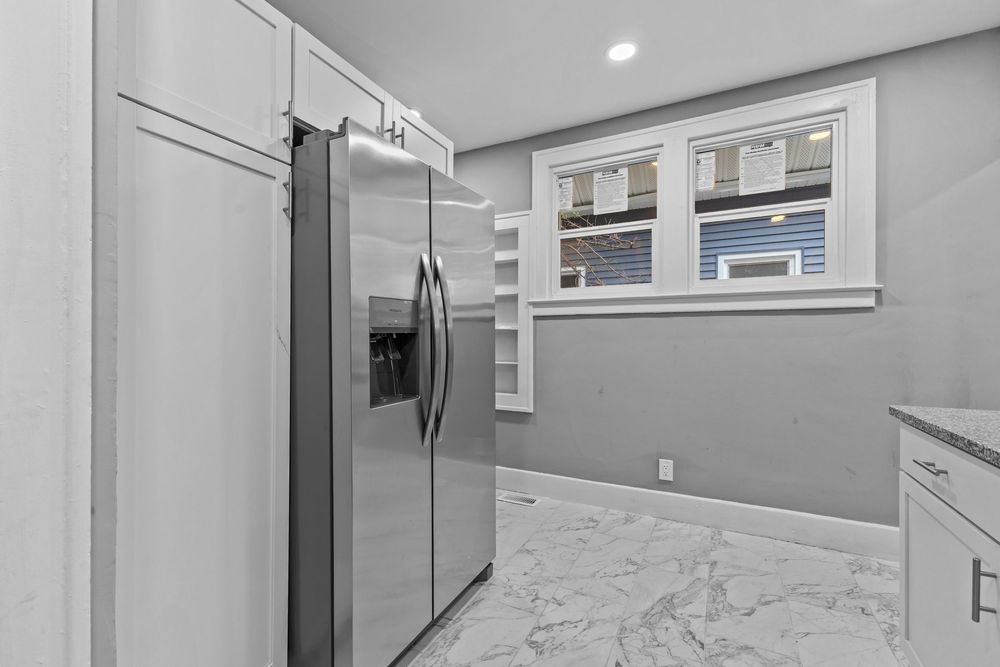 Modern kitchen featuring stainless steel French door refrigerator, marble tile floors, white cabinets, and a bright window. Detroit Michigan