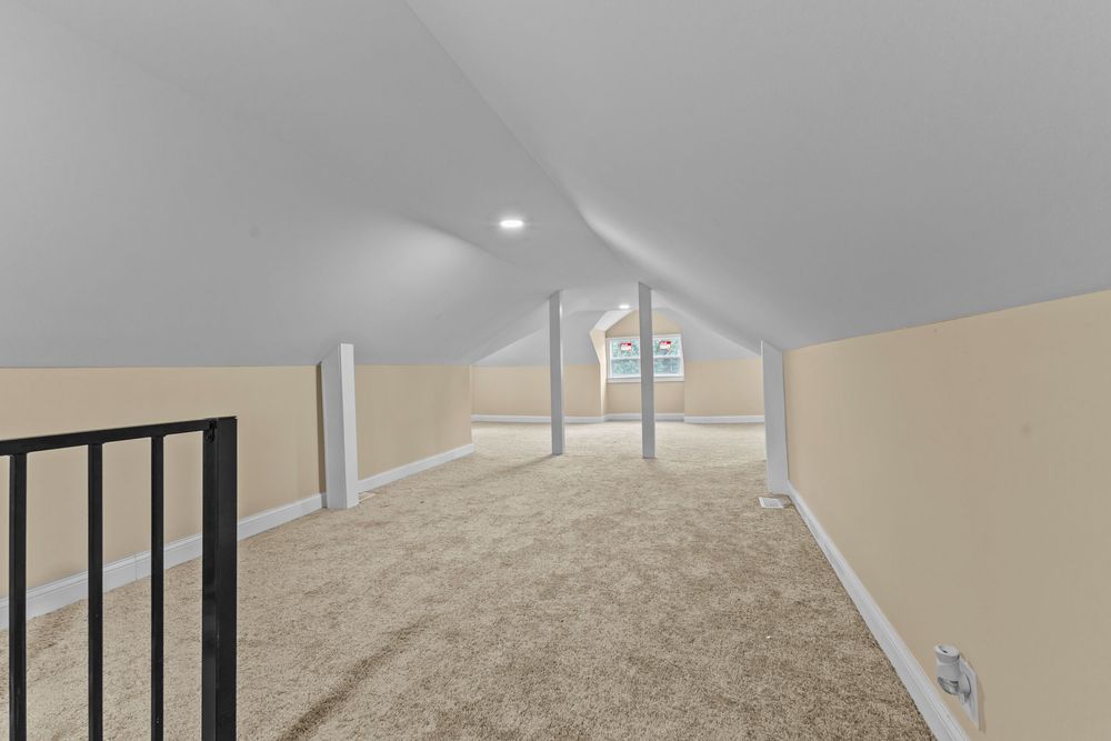 Spacious attic bonus room with sloped ceilings, neutral carpet flooring, and beige walls with white trim.