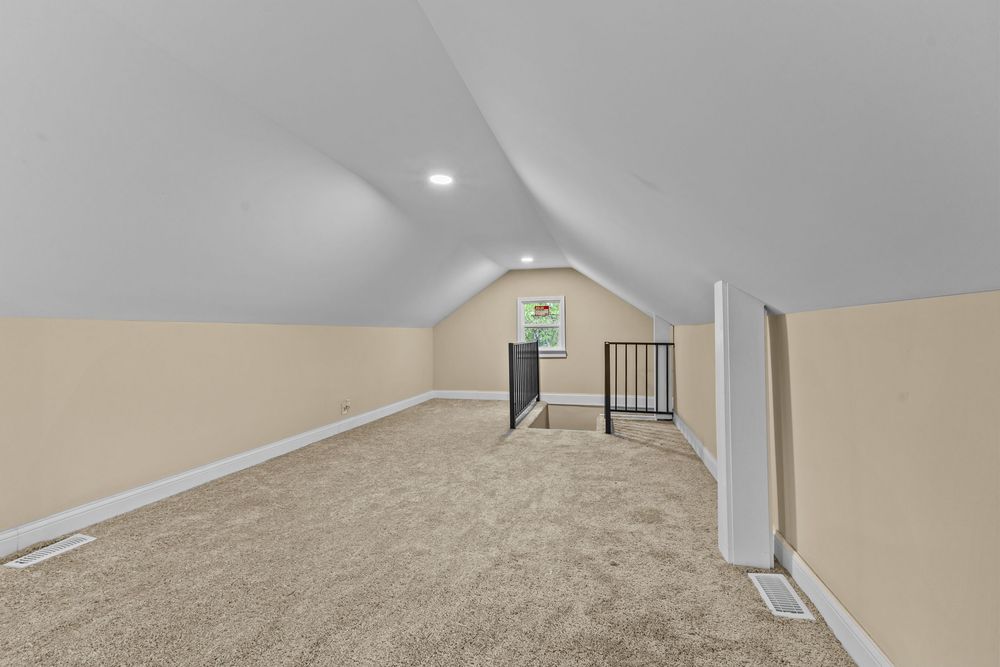 Spacious bonus room with vaulted ceiling, neutral carpet, cream walls, recessed lighting, and open staircase railing. Detroit Michigan Photo