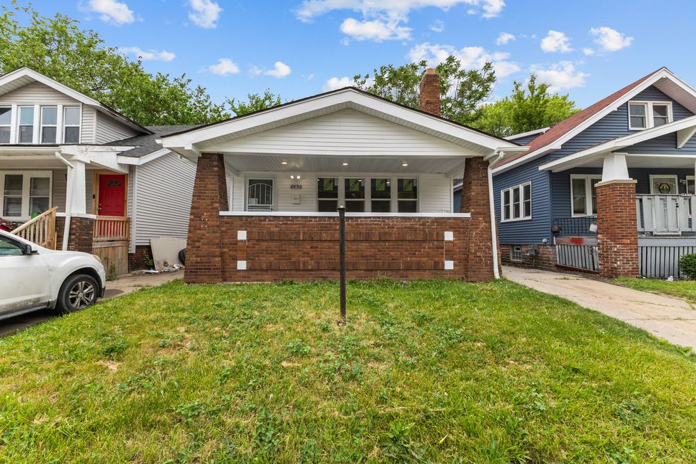 Charming brick bungalow with covered porch, lush green lawn, and mature trees in a residential neighborhood. Detroit Michigan Photo