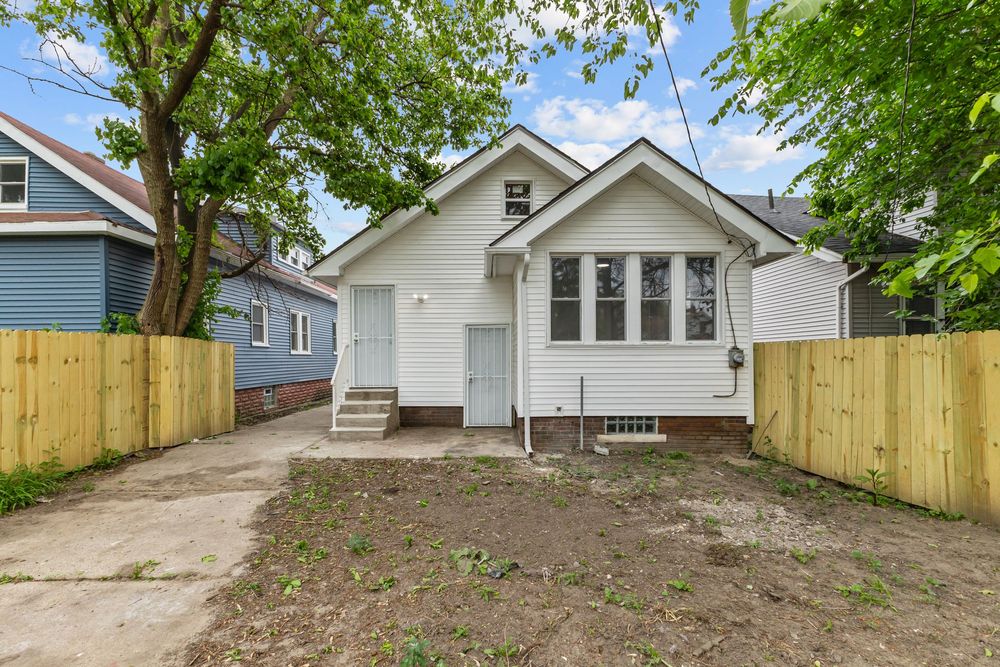 Small white bungalow with brick foundation, wooden fence, and mature trees in a residential neighborhood. Detroit Michigan Photo