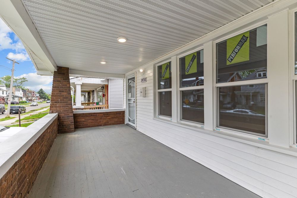 Spacious covered front porch with white siding, large windows, and recessed lighting on a residential home.