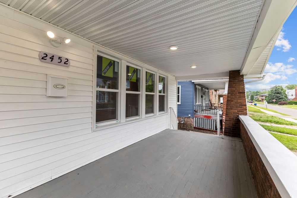 Covered front porch of house number 2952 with white siding, large windows, and a view of neighboring homes.