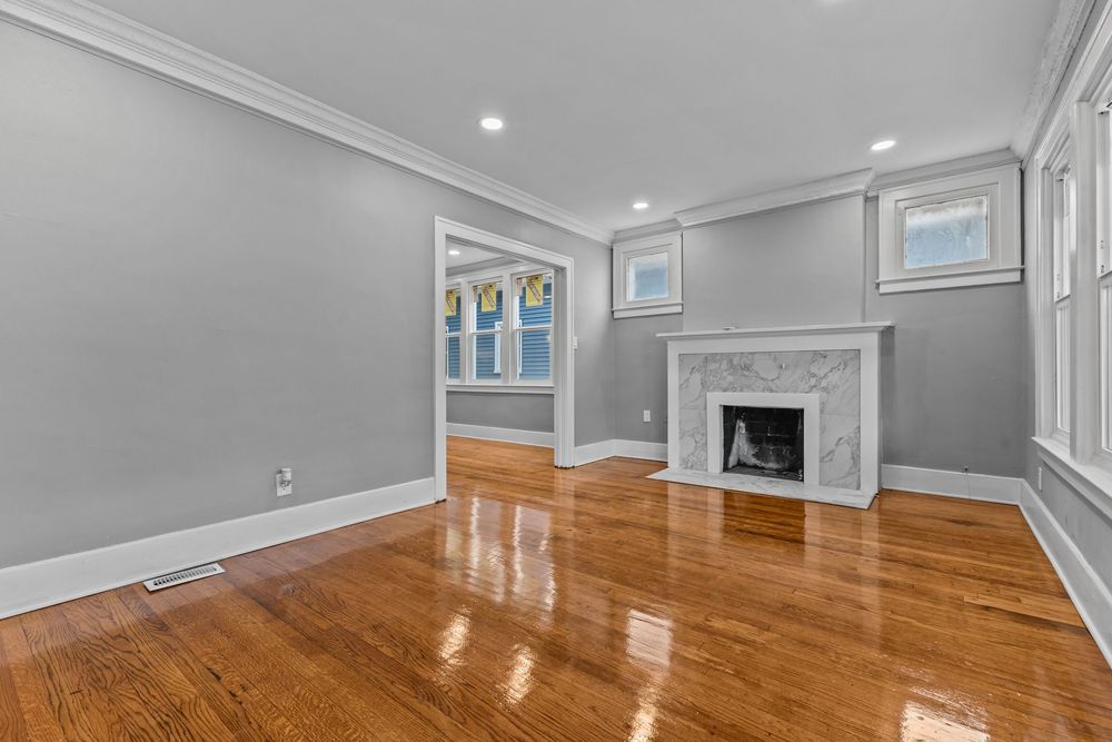 Bright living room with hardwood floors, marble fireplace, crown molding, and large windows in a classic home. Detroit Michigan Photo