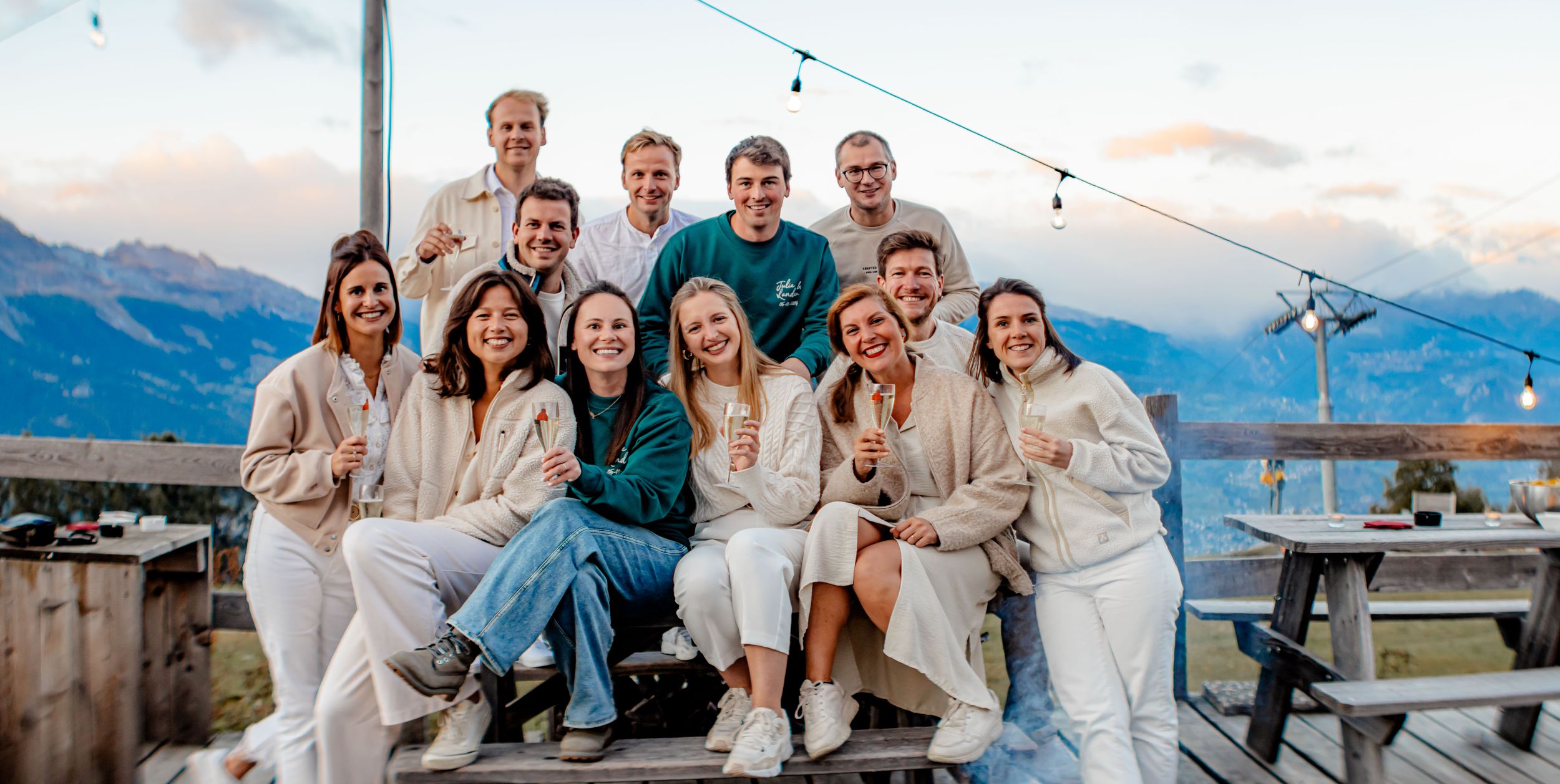 Group of friends in casual white and denim outfits gather on mountain deck during sunset with scenic views.