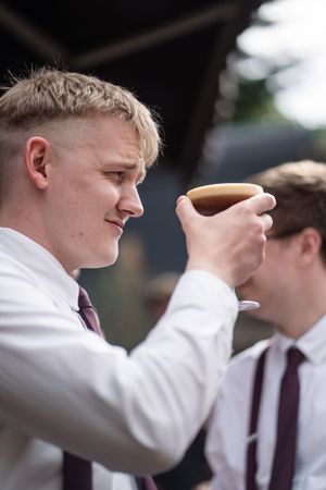 Young groomsman in white shirt and burgundy tie raising a espresso martini glass at wedding reception.