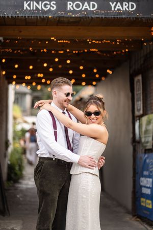 Couple in sunglasses embracing under string lights at Kings Road Yard on their wedding day.
