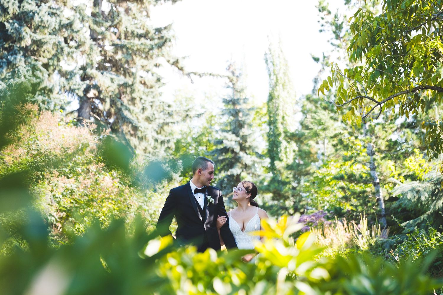 A bride and groom share a romantic moment surrounded by lush green trees and foliage on their wedding day.