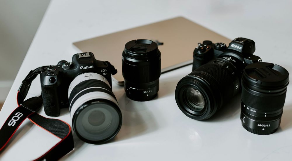 Two Canon EOS cameras with multiple lenses and a laptop on a white surface, professional photography equipment setup.