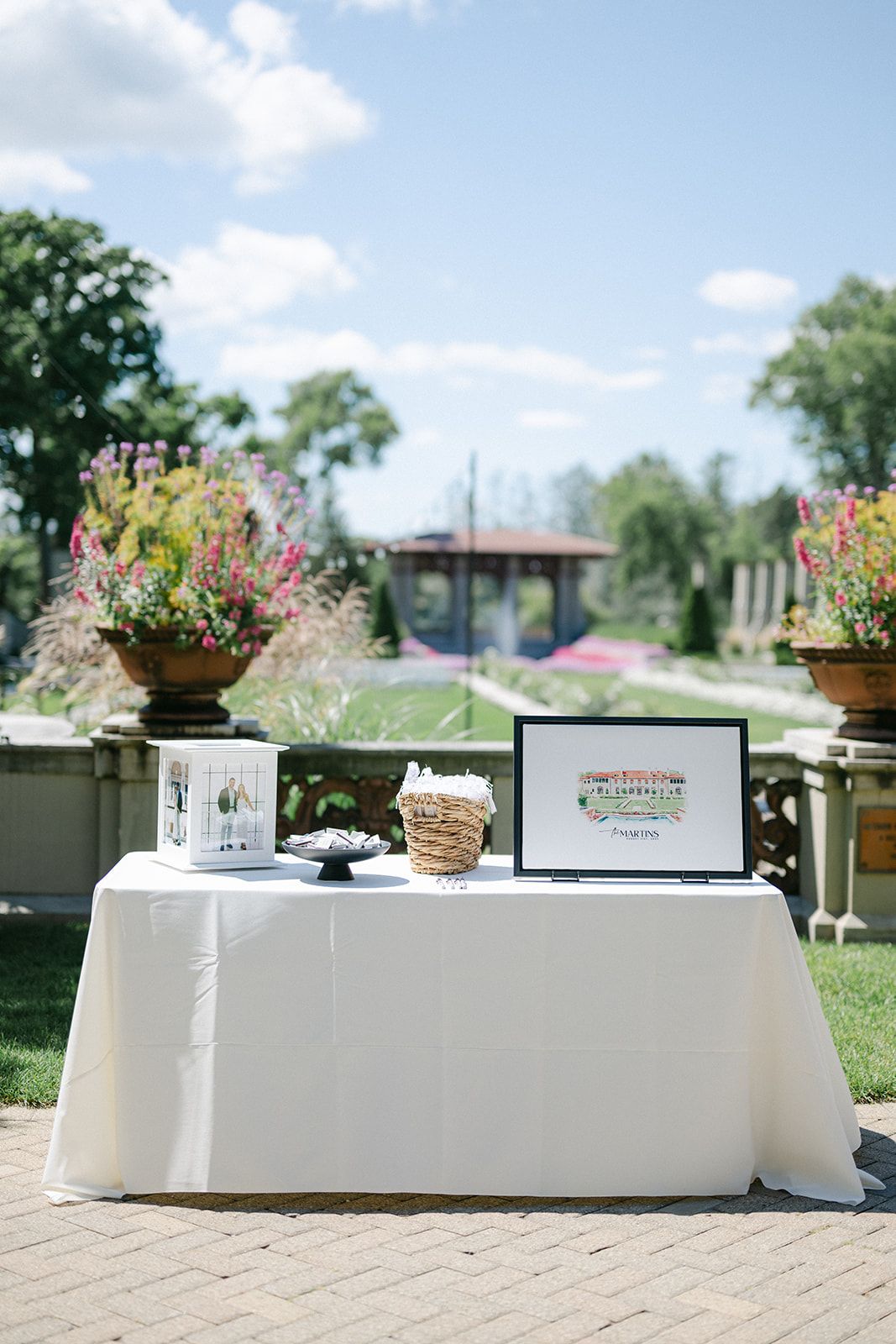 Armour House Wedding - Elegant outdoor wedding welcome table with white linen, framed art, lantern, and floral arrangements.