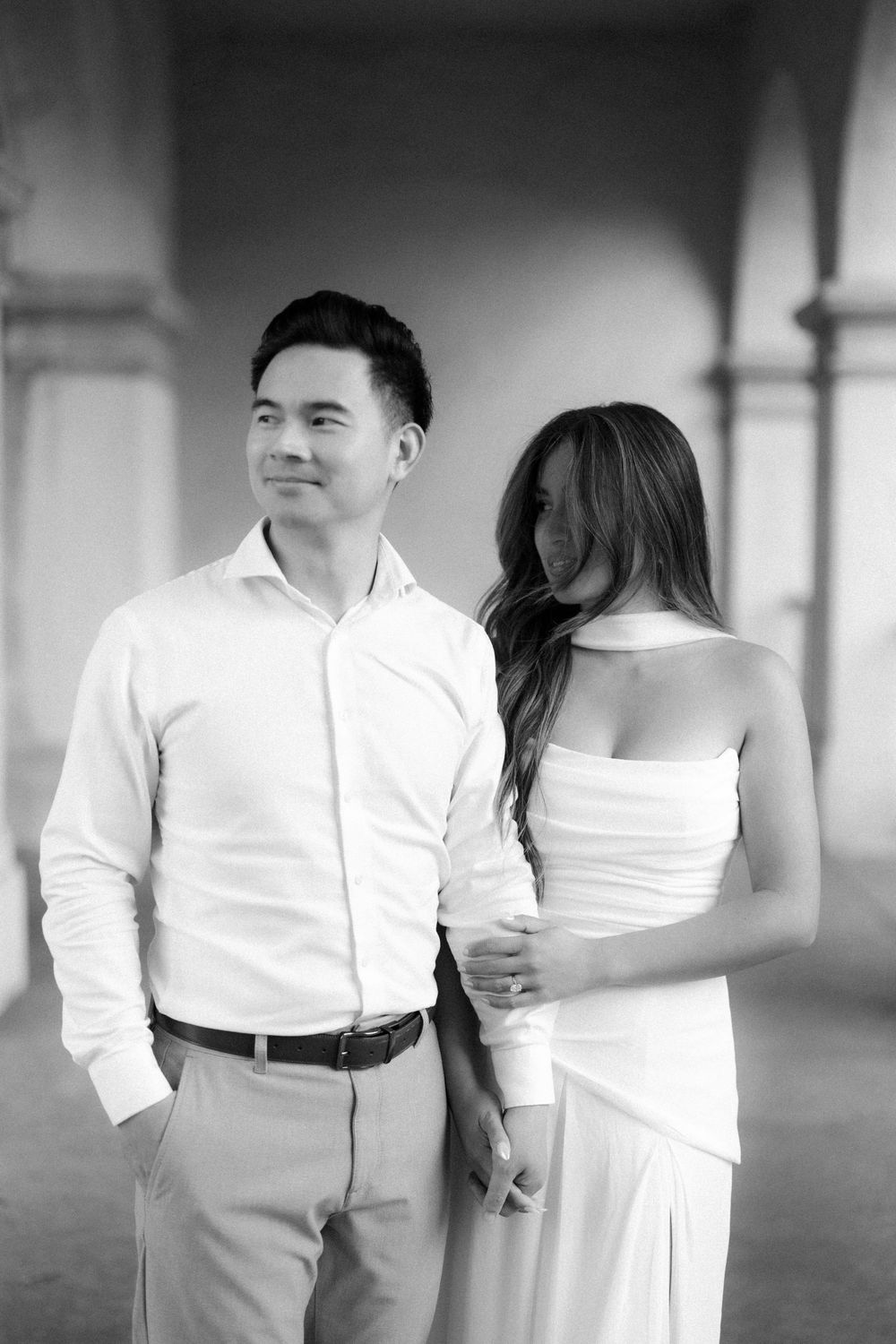 Black and white photo of an elegant couple in white attire standing together in an archway.