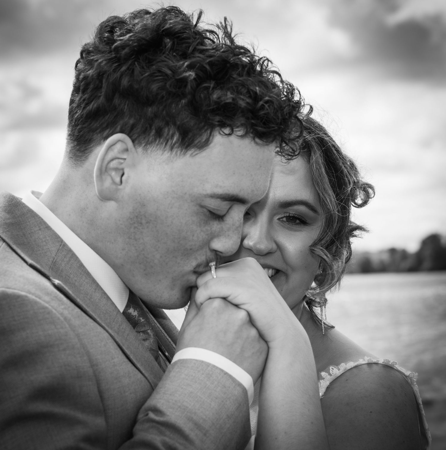 Black and white close-up of groom kissing bride's hand tenderly in an open field.