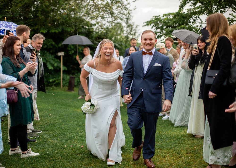 Smiling bride and groom walk hand-in-hand through a guest-lined garden aisle at an outdoor wedding ceremony.