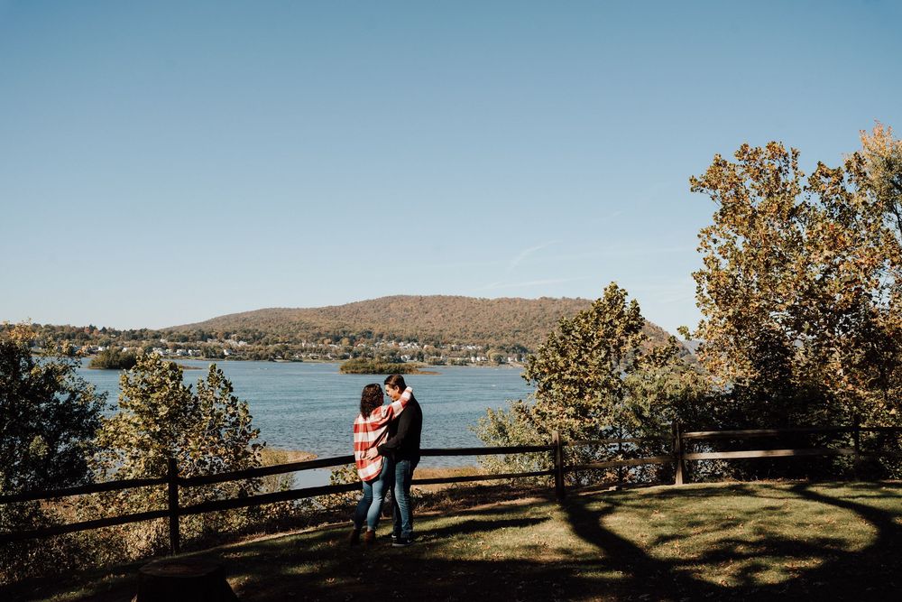 Couple embracing by a wooden fence overlooking a serene lake at Fort Hunter Mansion and Park for their engagement photos in Central PA