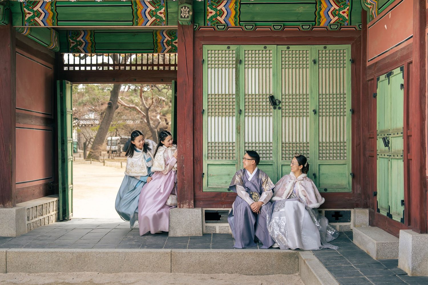Four women in traditional Korean hanbok attire sit and chat at a colorful palace pavilion in Seoul, South Korea.