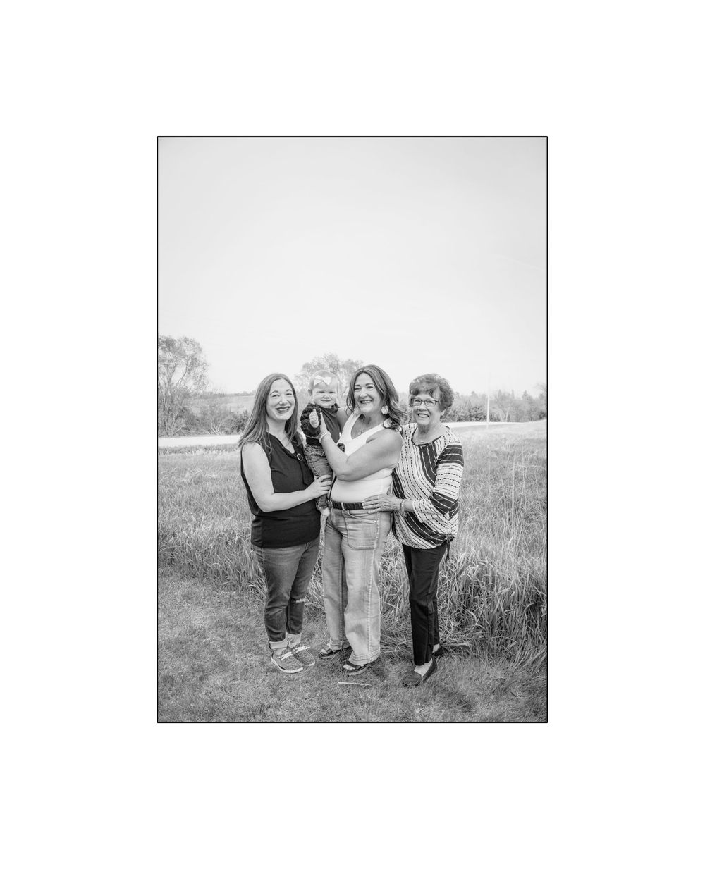 Black and white photo of three women and a baby posing together in a grassy field outdoors.