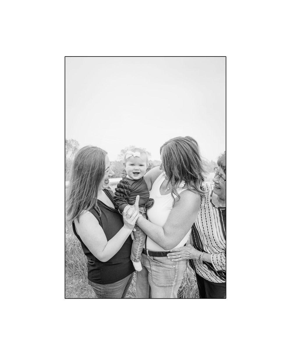 Black and white photo of two women smiling and holding a happy baby outdoors.