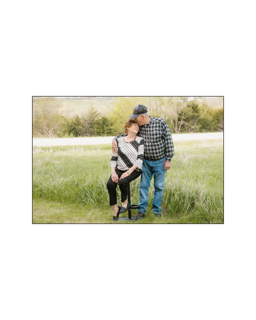 A couple shares a tender moment standing together in a lush green meadow.