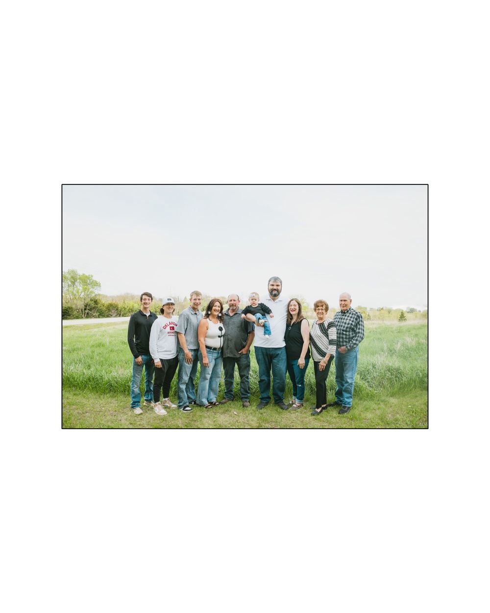 A large family group of ten people posing together outdoors in a green field on a sunny day.