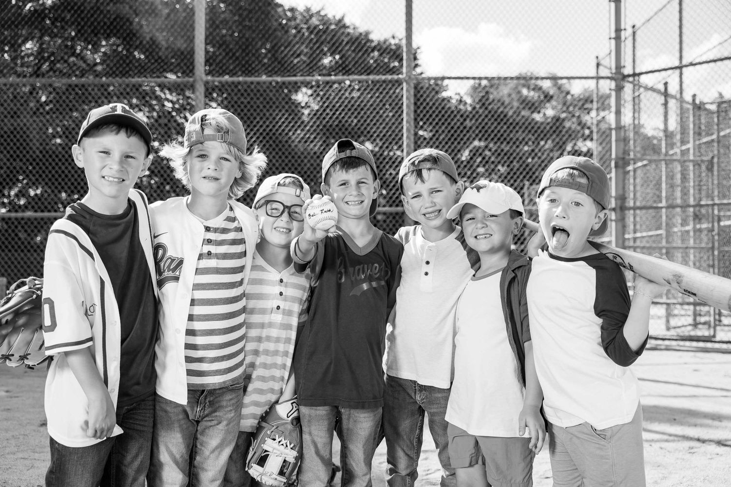 Group of seven young boys in baseball caps posing together and smiling at an outdoor sports court.