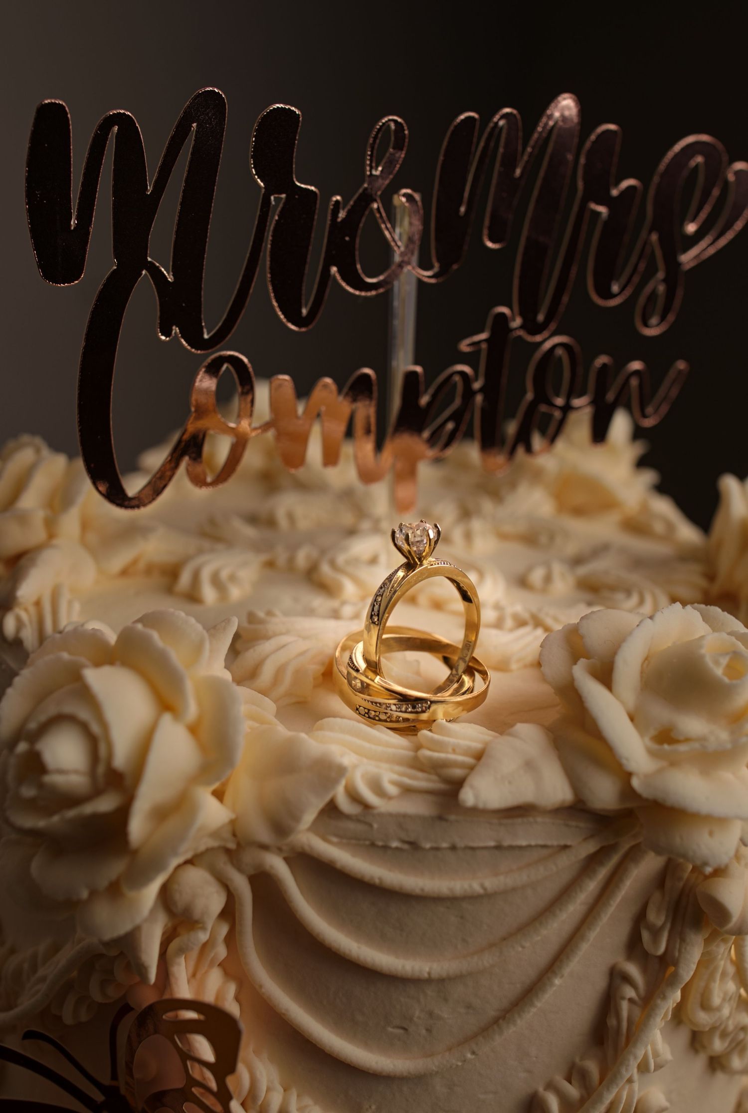 Gold wedding ring nestled in white frosting or cream on what appears to be a decorated cake surface.