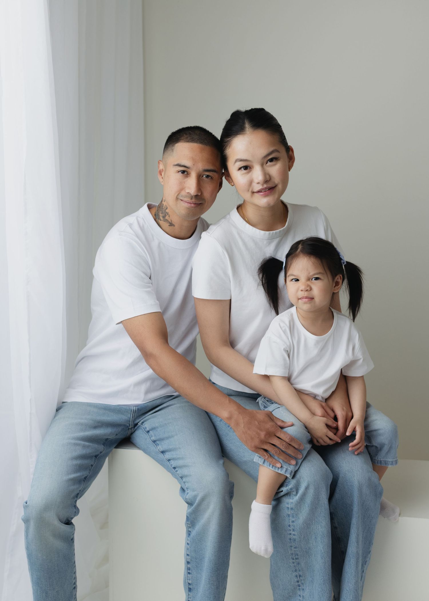 Family of three in matching white tees and jeans posing together for a portrait photo.