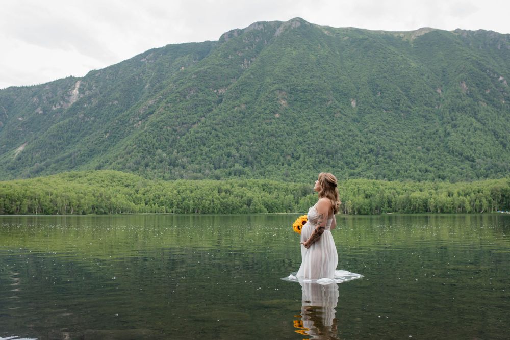 Person in flowing white dress standing in mountain lake for artistic maternity photo.