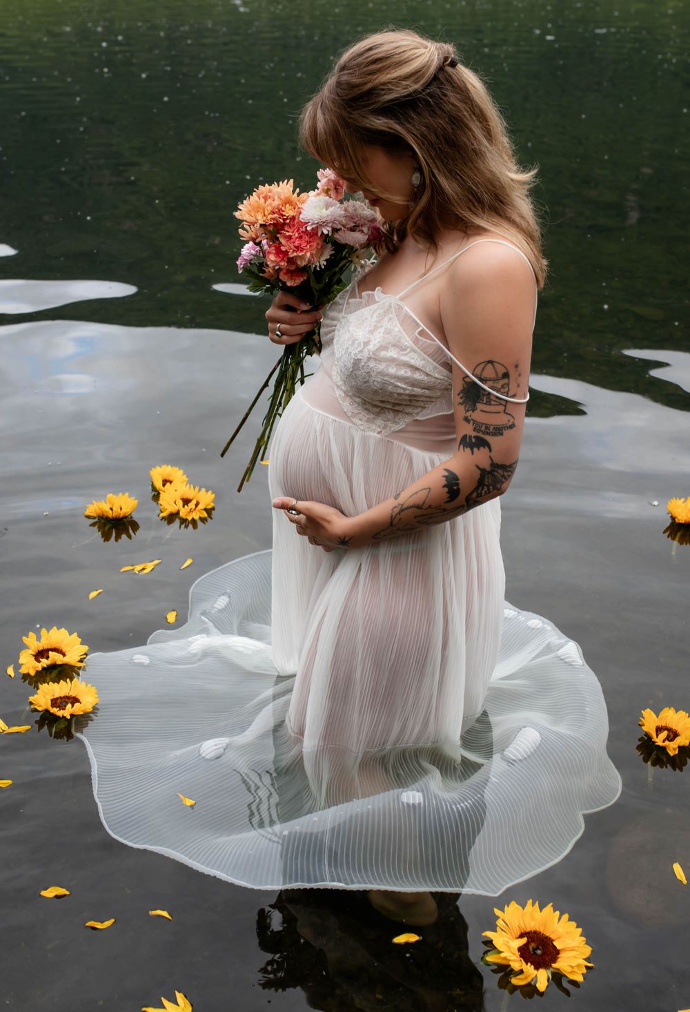 Maternity photo with sunflowers floating on water, white dress, and colorful bouquet.