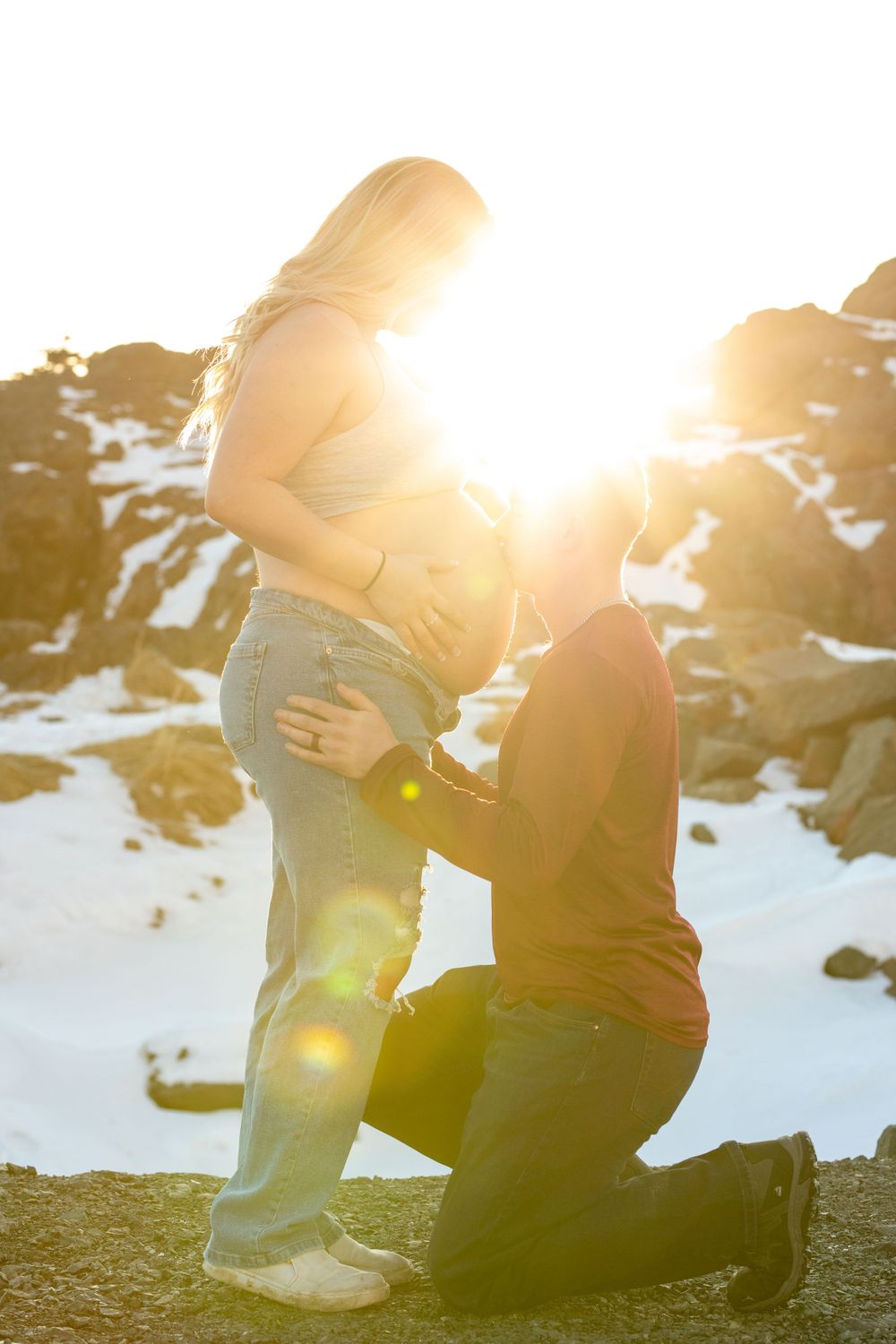 Romantic winter proposal scene with snowy mountains in background at sunset.