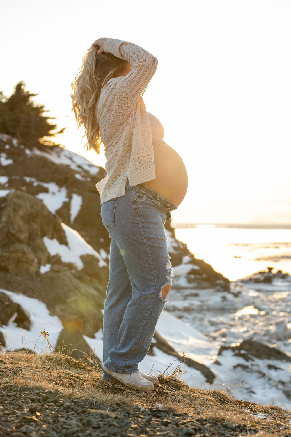 Side profile maternity photo at sunset with snowy coastal landscape.