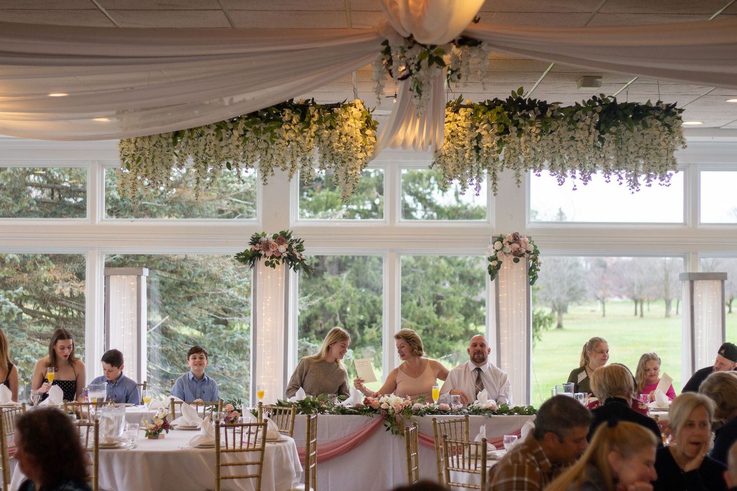 A panoramic view of an elegant wedding reception venue with white floral decorations hanging from the ceiling.