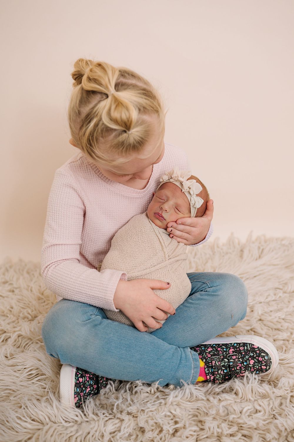 Tender moment showing parent cradling swaddled newborn on fluffy white rug.