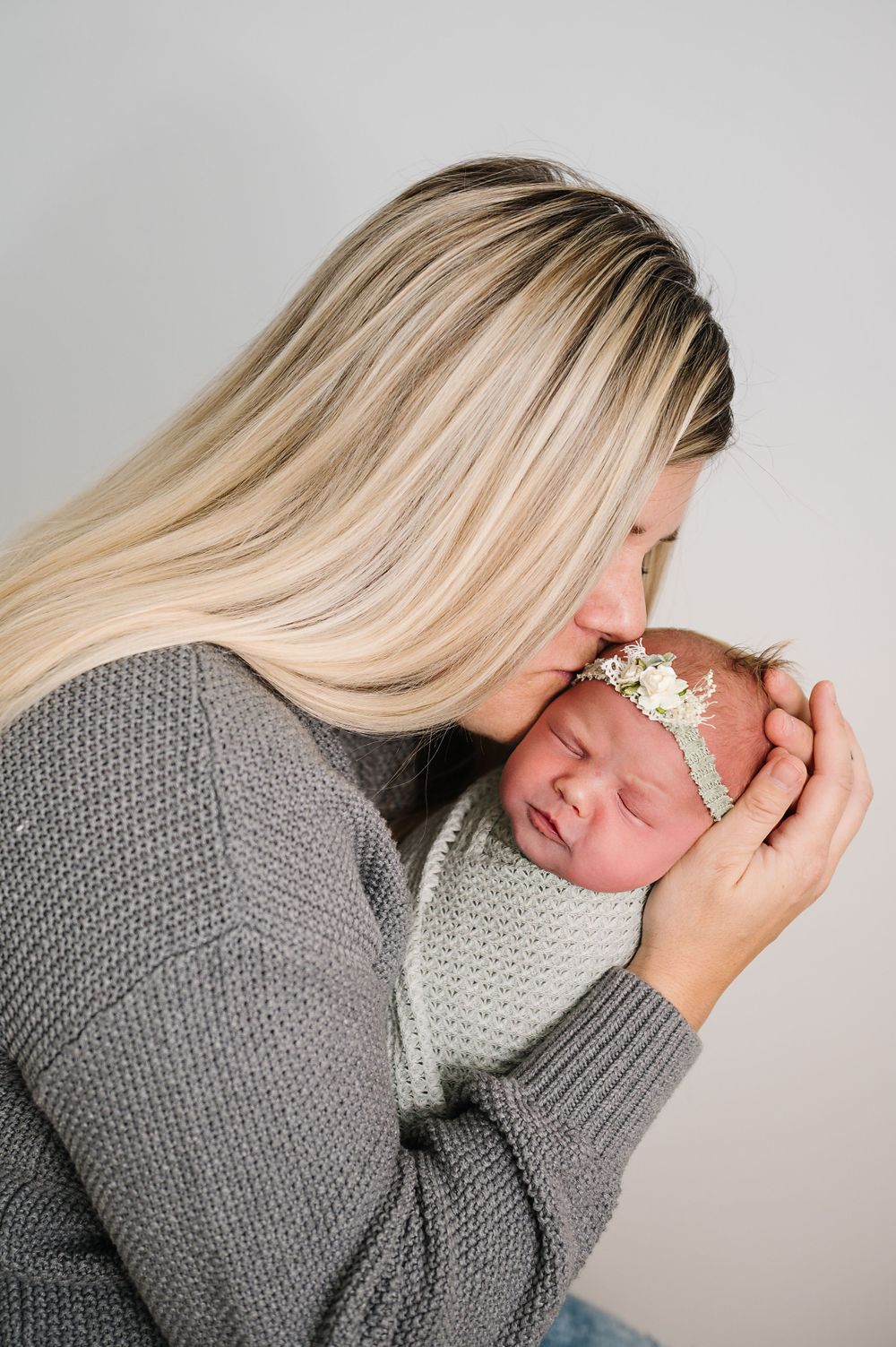 Tender moment between parent and newborn in gray knit sweaters against neutral background.