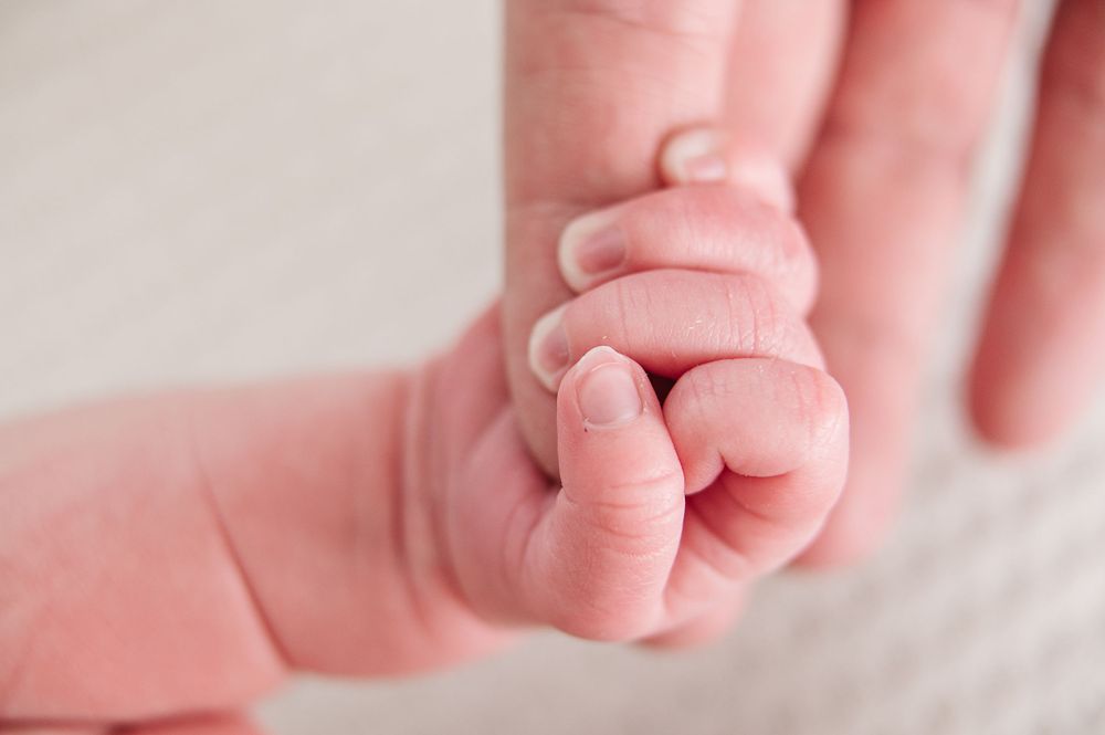 Close-up of tiny newborn hand grasping adult finger in soft pink lighting.