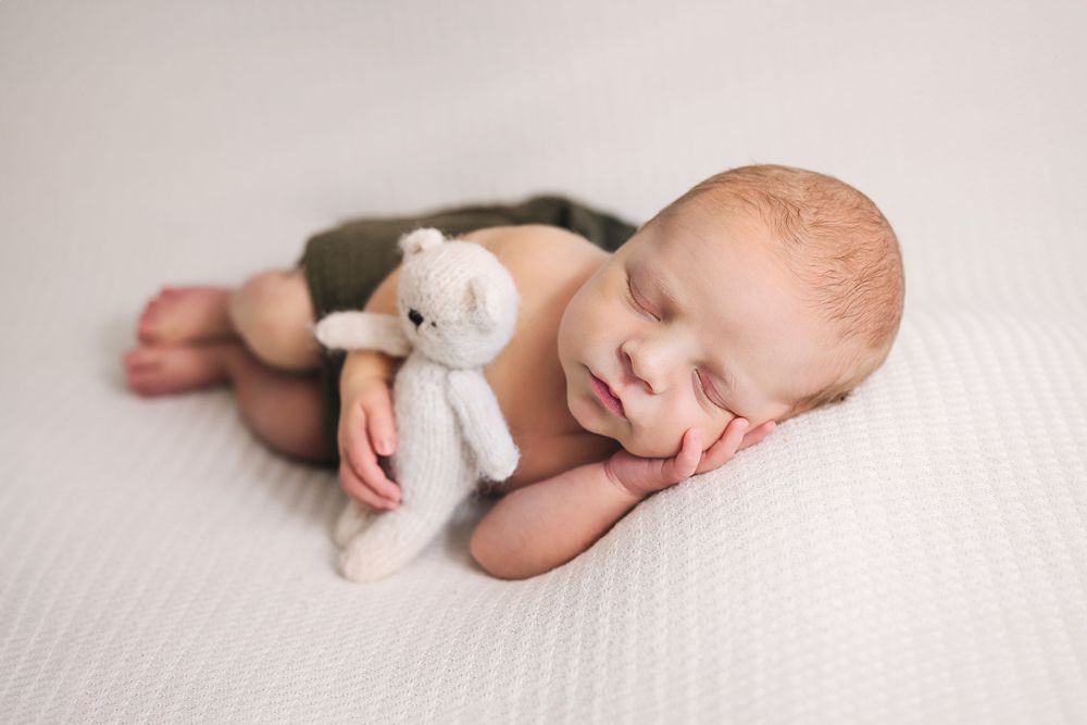 A peaceful newborn baby sleeping with a small stuffed animal on white bedding.