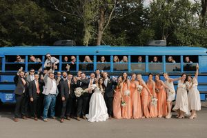 A wedding party poses in front of a bright blue school bus with bridesmaids in peach dresses.