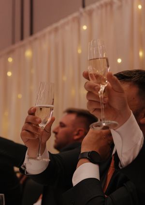 Guests raise champagne glasses for a toast during a wedding celebration with twinkling lights in the background.