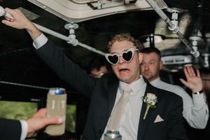 Party guest in sunglasses and black suit with boutonniere celebrates on a party bus by holding the ceiling rails.