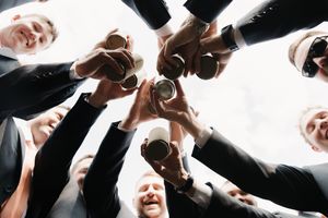 Business colleagues in formal wear joining wine glasses together in a celebratory toast from below perspective.